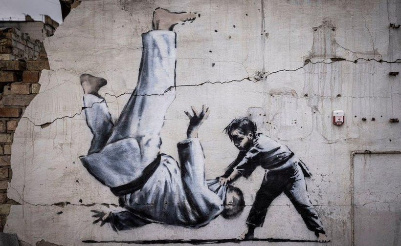 it's a banksy mural on a wall that's showing a kid doing a toss on an older person. They're wearing Gi's like they're doing martial arts.