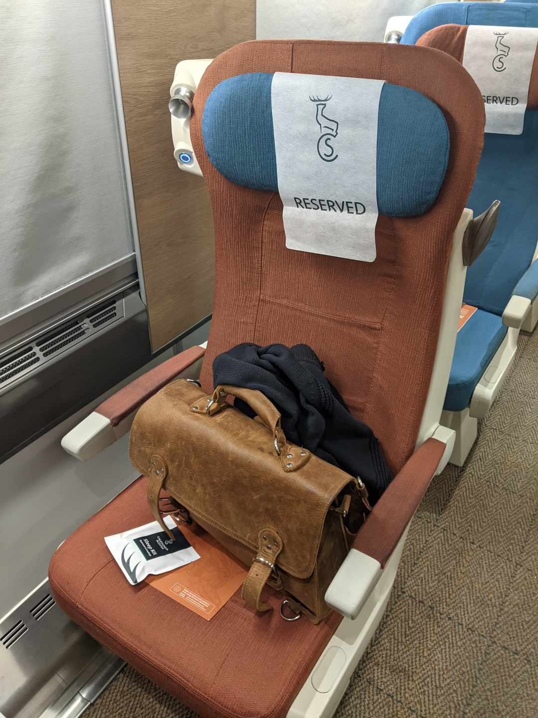 A photograph of a seat on a train, with a large leather briefcase on it.