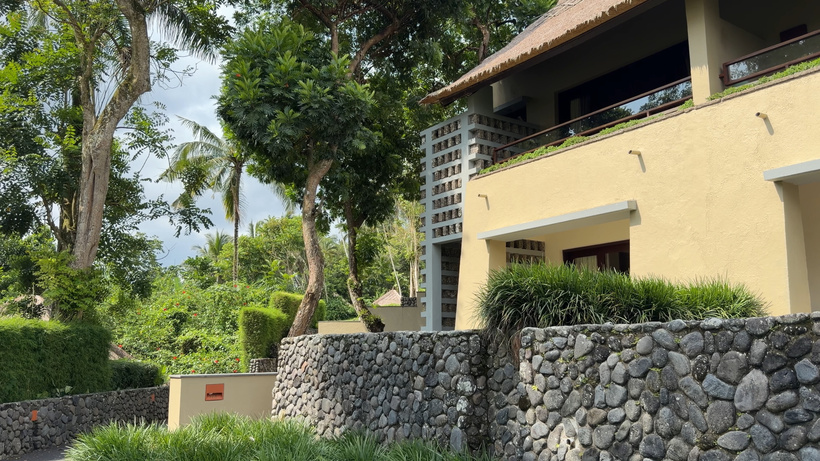 Exterior of a Deluxe room building at Alila Ubud with a river-stone wall base and tropical trees
