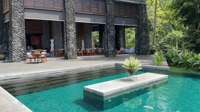 Poolside restaurant at Alila Ubud with wooden tables under a stone-pillared pavilion beside a turquoise pool