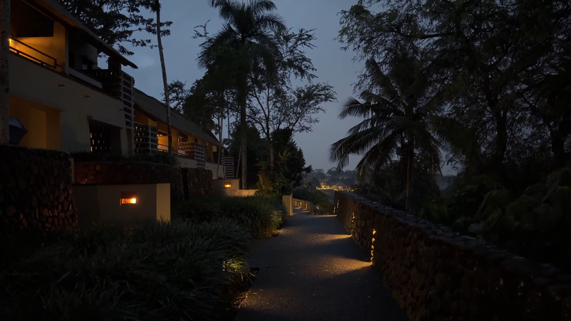 Lamp-lit stone pathway at night beside a wall, palm trees and resort buildings at Alila Ubud