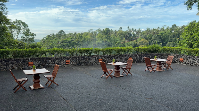 Outdoor terrace tables and chairs at Plantation restaurant beside a stone wall with jungle views at Alila Ubud