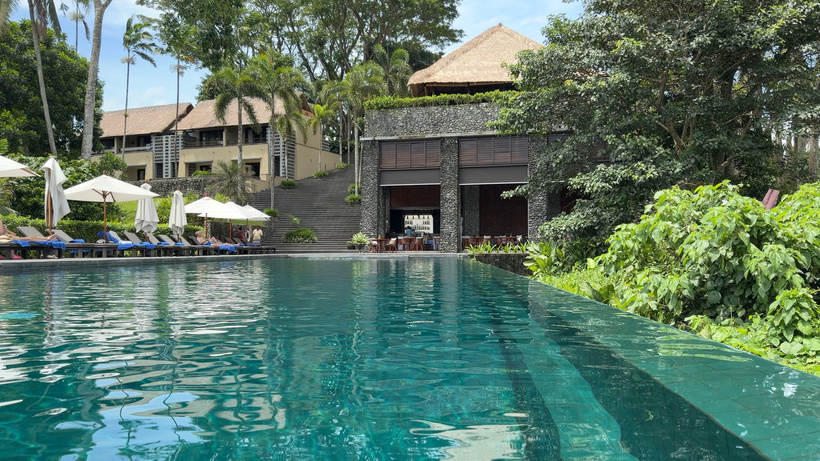 Turquoise infinity pool at Alila Ubud with white parasols, sun loungers and thatched resort buildings behind
