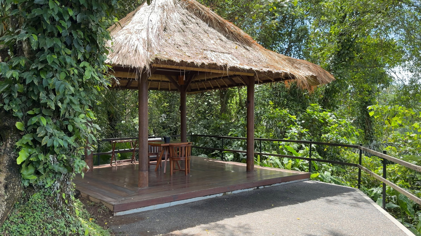 Bale Bengong Thatched wooden pavilion with a table and chairs on a paved terrace surrounded by jungle at Alila Ubud