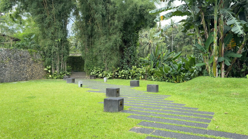 Grass lawn with a path of dark stepping stones leading toward bamboo and tropical plants at Alila Ubud