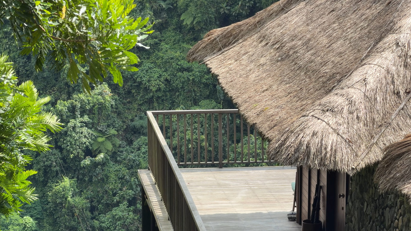 Thatched roof and wooden deck with a railing above dense jungle of Valley View Villa at Alila Ubud