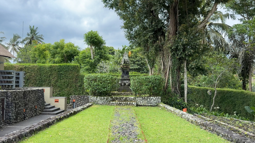 Green lawn with a stone path, low hedges and a small shrine statue at the far end, with stone steps on the left at Alila Ubud