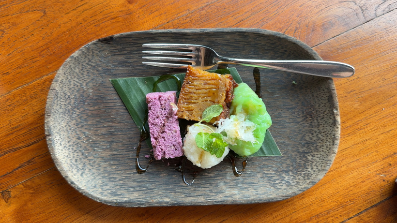 Plate of colourful Balinese sweet snacks in purple, green and white on a banana leaf with a fork on a wooden table