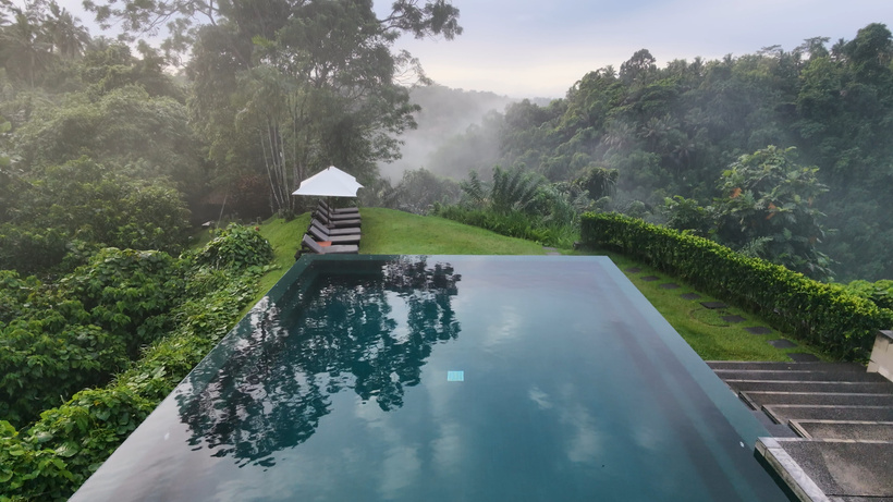 Alila Ubud infinity pool overlooking the misty Ayung River valley, with a white umbrella on the lawn beside it