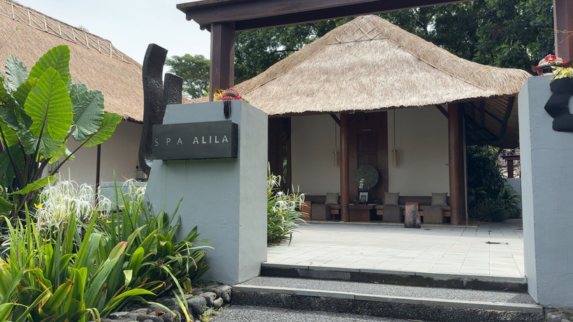 Entrance to Spa Alila with a grey sign, stone steps, a thatched roof and tropical plants