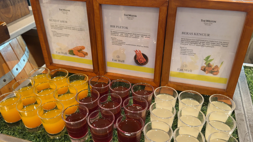 Rows of small glasses of orange, red and cream-coloured juices in front of three framed menu cards.