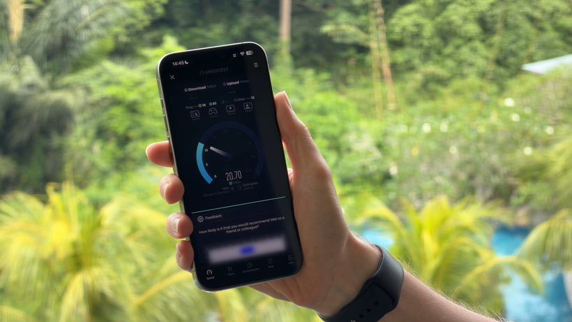 Hand holding a smartphone showing an internet speed test, with the resort's greenery and pool in the background.