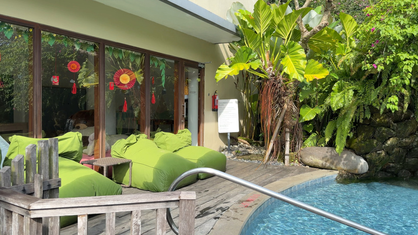 Kids' club terrace with green bean bags on a wooden deck beside the small children's pool and tropical plants.