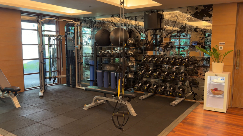 Gym with a dumbbell rack, weight bench, exercise balls, kettlebells and a suspension trainer on rubber flooring.