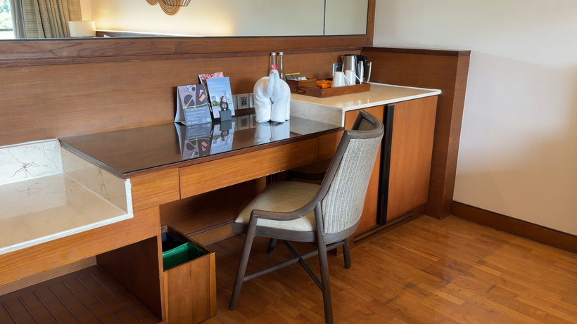Wooden desk and minibar area with a cushioned chair, a kettle and amenity items on the counter.