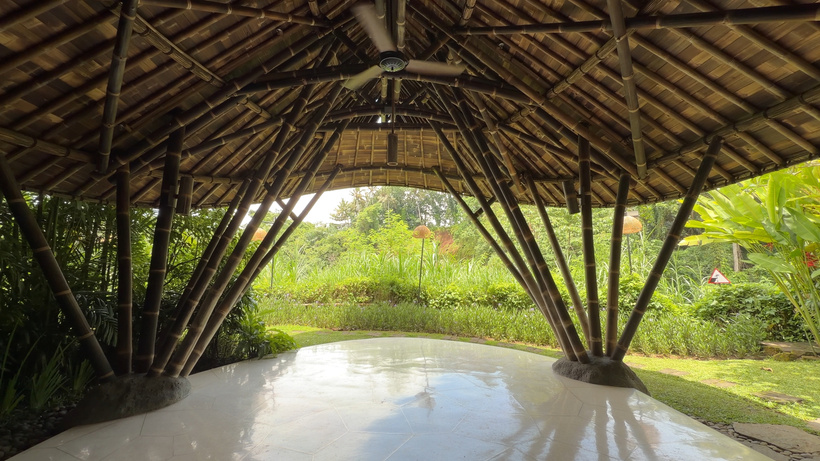 Open-air Yoga Hale with a thatched bamboo roof and a smooth pale floor looking onto a green garden.