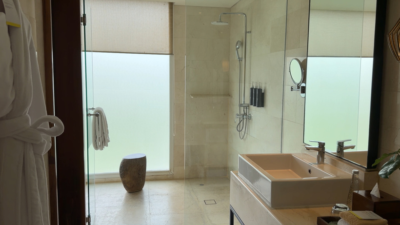 Bathroom with a frosted window, a white robe on the door, a wooden stool and a rectangular basin.