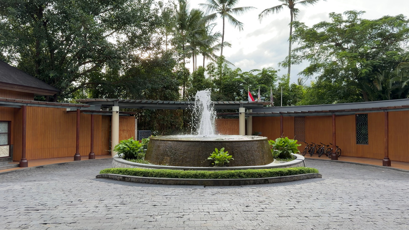 Paved circular entrance driveway and fountain at The Westin Ubud with parked bicycles and jungle foliage under palm trees.