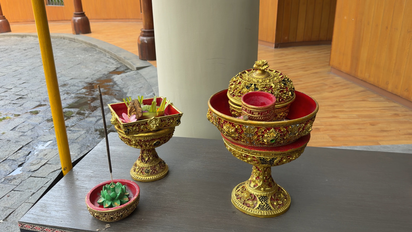 Balinese welcome ritual setup with incense, flowers, and ornate red and gold decorative offering bowls.