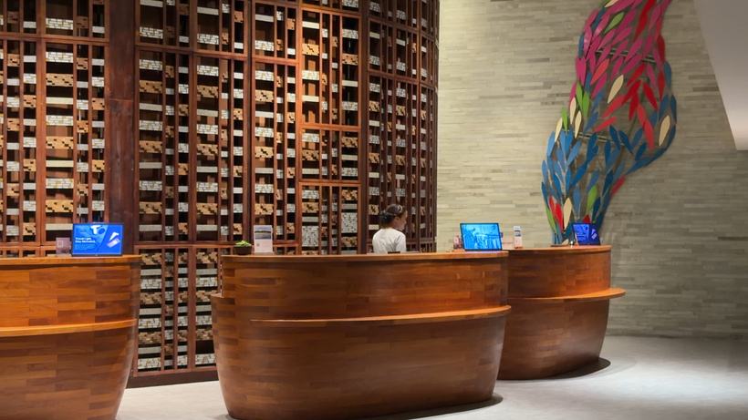 Curved wooden reception desks in the Westin Ubud lobby with a wall of wooden shelving and a colourful glass artwork behind.