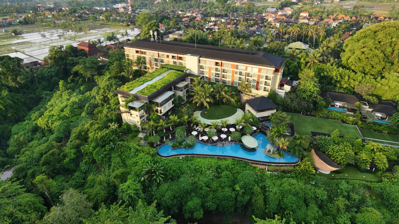 Aerial view of the multi-story Westin Ubud resort nestled in dense jungle with terraced pools and background rice paddies.